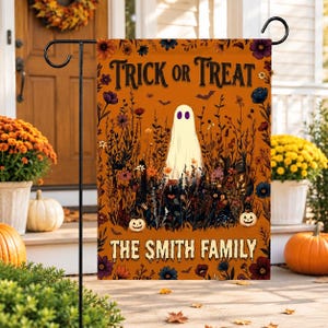 Könnte beinhalten: Eine rechteckige orangefarbene Gartenflagge mit einem zentralen weißen Geist mit violetten Augen, umgeben von dunklen Blumenillustrationen, Fledermäusen und zwei kleinen Kürbissen. Der Text lautet TRICK OR TREAT oben und THE SMITH FAMILY unten.