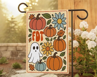May include: A garden flag featuring a retro design with pumpkins, flowers, and a ghost. The flag has the letters "FDT" in orange. The background is a light beige with a grid pattern. The flag is displayed on a black metal stand.