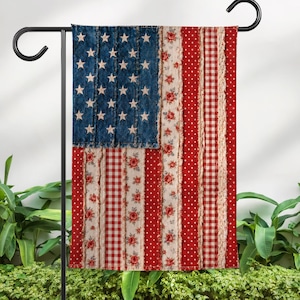 May include: A decorative garden flag featuring the American flag design. The flag has a blue section with white stars, and red and white stripes with floral and polka dot patterns. The flag is hanging on a black metal stand.
