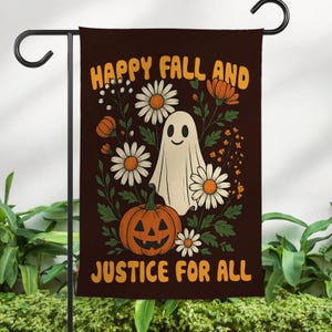 May include: A decorative garden flag with a brown background features a smiling ghost, jack-o'-lantern, and daisies. The text "HAPPY FALL AND JUSTICE FOR ALL" is displayed in orange. The flag is hanging on a black metal pole.