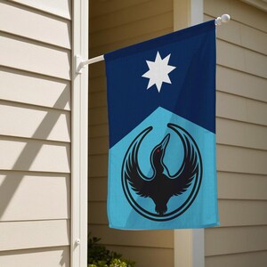Op de afbeelding: Een rechthoekige vlag voor buiten met een geometrisch ontwerp. Het bovenste gedeelte is donkerblauw met een witte ster. Het onderste gedeelte is lichtblauw met een zwart vogel-embleem in een cirkel.