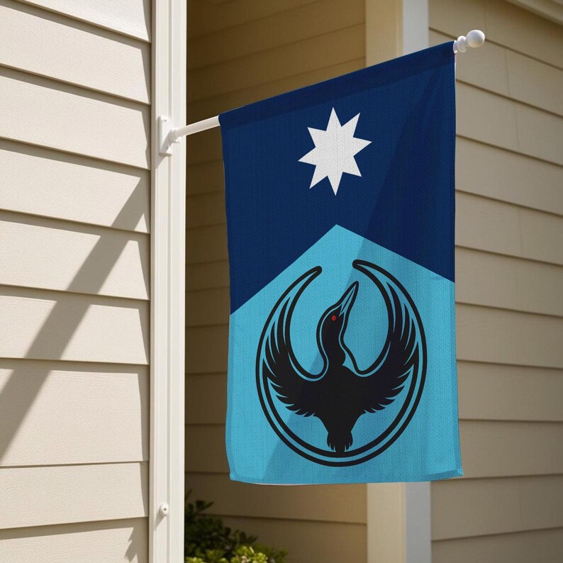 Op de afbeelding: Een rechthoekige vlag voor buiten met een geometrisch ontwerp. Het bovenste gedeelte is donkerblauw met een witte ster. Het onderste gedeelte is lichtblauw met een zwart vogel-embleem in een cirkel.