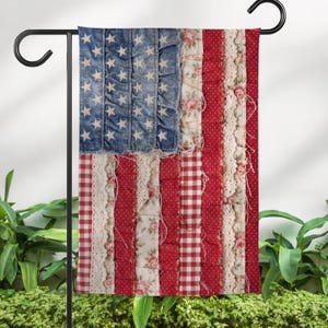May include: A decorative garden flag featuring a patchwork design of the American flag. The flag has a denim blue section with white stars, red and white stripes, and floral and lace accents. The flag is displayed on a black metal stand.