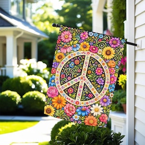 May include: A rectangular garden flag featuring a central white peace sign emblem surrounded by a dense, colorful pattern of various flowers including pink, yellow, orange, and blue blossoms against a dark background, hanging from a black pole.