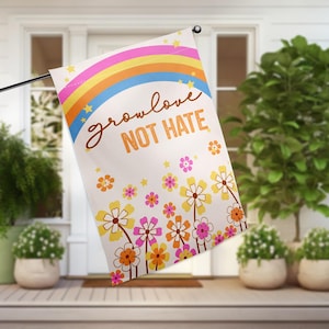 May include: A white garden flag with a rainbow, stars, and flowers. The text on the flag reads "grow love not hate".