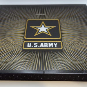 May include: A black square plaque with a gold star and the words "U.S. ARMY" in gold lettering. The background is a black and gold radial pattern.