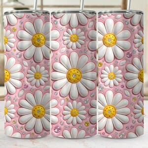 Pode incluir: Três canecas rosas com um padrão de margaridas. As margaridas têm pétalas brancas e centros amarelos, com pequenos strass espalhados. As canecas têm uma borda prateada e um canudo.