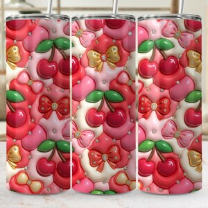 May include: A stainless steel tumbler featuring a colourful pattern of cherries, bows, and heart shapes in red, pink, and white. The design includes gold bows and sparkling accents, creating a decorative look. The tumbler has a straw.
