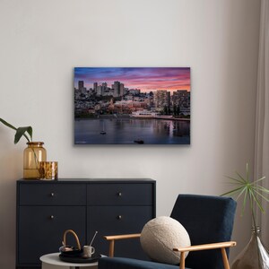 a cityscape with a river and boats, as depicted in a framed artwork hanging on the wall.
