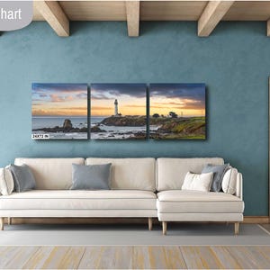 May include: A three-panel canvas print depicting a lighthouse on a rocky coastline. The print features a sunset sky with warm colors and a calm ocean. The print is displayed on a white couch in a living room setting.