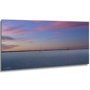 May include: A panoramic landscape photograph featuring a calm body of water under a twilight sky with soft pink and blue clouds. Two small sailboats are visible in the distance on the horizon line. The signature John Beatty Photography is visible.