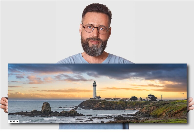 May include: A panoramic photograph of a white lighthouse on a rocky coastline with a dramatic sunset sky. The lighthouse is located on a small island with a few buildings and trees. The water is calm and the sky is a mix of orange, pink, and purple.