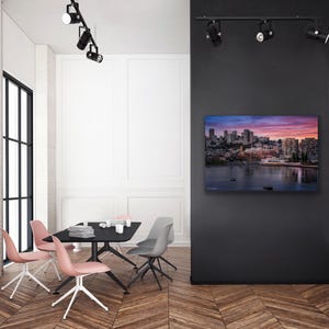a modern, minimalist living room with a large black wall as the focal point. On the wall, there is a framed image of a city skyline at sunset. The room is furnished with a black dining table surrounded by four chairs, and a flat-screen TV is mounted on the wall. The overall design and color scheme of the room create a sleek and sophisticated atmosphere.