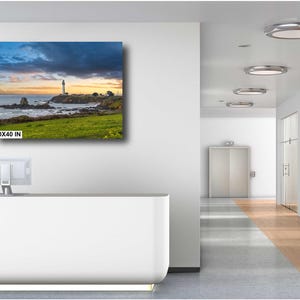 May include: A canvas print of a lighthouse on a rocky coastline with a dramatic sky. The print is 30x40 inches and is displayed on a white wall in a modern office setting.