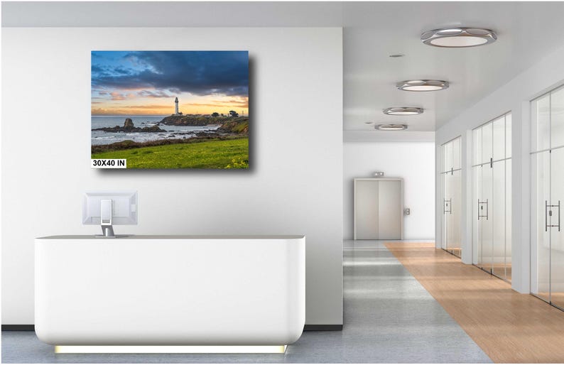 May include: A canvas print of a lighthouse on a rocky coastline with a dramatic sky. The print is 30x40 inches and is displayed on a white wall in a modern office setting.