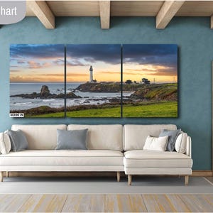 May include: A three-panel canvas print of a seascape with a lighthouse in the distance. The sky is a vibrant orange and pink, and the water is a deep blue. The canvas is hung on a wall in a living room setting.