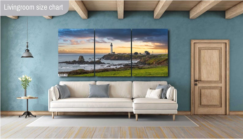 May include: A three-panel canvas print of a seascape with a lighthouse in the distance. The sky is a vibrant orange and pink, and the water is a deep blue. The canvas is hung on a wall in a living room setting.