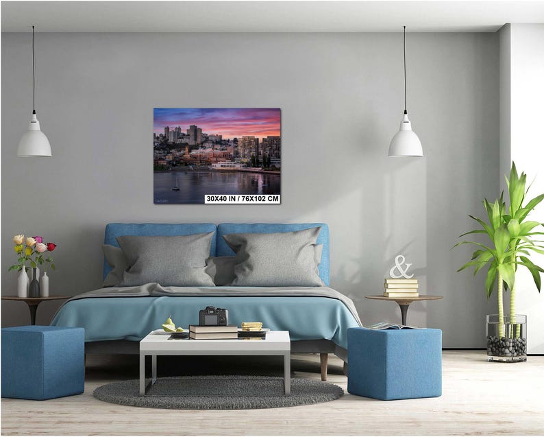 a modern bedroom with a large bed, a coffee table, and a potted plant. The room has a minimalist and contemporary design, with a gray color scheme and white lighting fixtures.