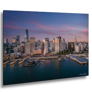 May include: An aerial view of the San Francisco skyline at dusk. The image showcases a vibrant sunset with shades of pink and blue. The city's skyscrapers and waterfront are visible, with the Transamerica Pyramid and Salesforce Tower prominent.
