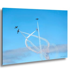May include: A photograph of five aeroplanes performing an air display in a clear blue sky. The planes, leaving white vapour trails, create a large looping pattern. One plane is red, while the others are black.