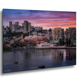 a cityscape with tall buildings and a body of water in the foreground, with a colorful sunset sky in the background.