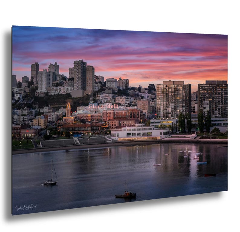 a cityscape with tall buildings and a body of water in the foreground, with a colorful sunset sky in the background.