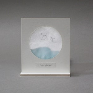 Può includere: Un biglietto bianco con un'immagine circolare di due volti e uno sfondo blu e bianco. Il biglietto ha la parola "interlude" scritta su di esso.