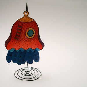 Könnte beinhalten: Ein rotes und blaues Papierbastel-Ornament in Form einer Glocke mit einem Bullauge und einer Leiter. Das Ornament steht auf einem Drahtständer.