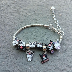 May include: A silver charm bracelet featuring black and white cartoon characters, including a charm that reads "Kuromi".