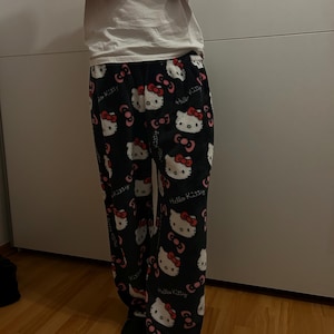 Pu&ograve; includere: Pantaloni da pigiama neri con stampa bianca di Hello Kitty. I pantaloni hanno un fiocco rosso e un viso bianco.