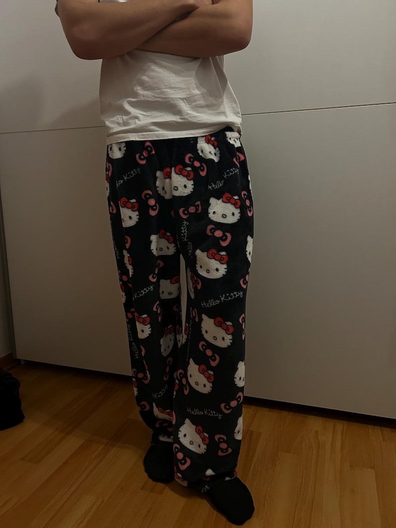 Pu&ograve; includere: Pantaloni da pigiama neri con stampa bianca di Hello Kitty. I pantaloni hanno un fiocco rosso e un viso bianco.
