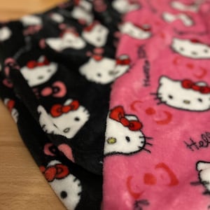 Pu&ograve; includere: Pigiama in pile nero e rosa con stampa Hello Kitty. Il pigiama presenta un lato nero con facce di Hello Kitty bianche e un lato rosa con facce di Hello Kitty bianche e il testo "Hello Kitty".