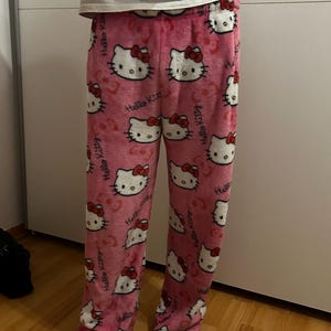 Pu&ograve; includere: Pantaloni da pigiama rosa Hello Kitty con sfondo bianco e un motivo ripetuto di volti Hello Kitty.
