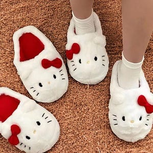 May include: Three pairs of white fuzzy slippers with red bows and a Hello Kitty face design.