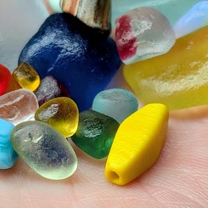 Puede incluir: Una colección de piezas de vidrio de mar lisas y coloridas de varias formas y tamaños. El surtido incluye piezas en tonos azules, rojos, amarillos, verdes y transparentes, con algunas piezas que muestran patrones internos. El vidrio tiene un aspecto esmerilado.