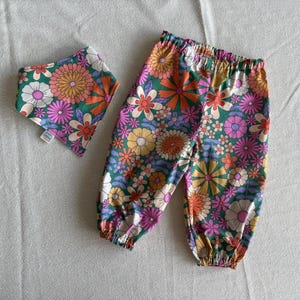May include: A pair of green, pink and orange floral print trousers with a matching bib. The trousers have an elastic waistband and a relaxed fit.