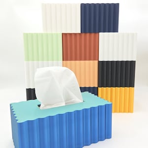 May include: A blue tissue box with a wavy top, holding white tissues. Behind it are several corrugated rectangular blocks in various colors: white, navy, green, brown, orange, black, and yellow. The blocks have a textured, ridged design.