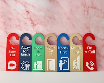 May include: A set of six colorful door hangers with various messages and icons. The hangers are red, navy, green, tan, blue, and red. Text includes "On Zoom Call," "Away for lunch," "Room In Use," "Come On In," "Knock First," and "On A Call."