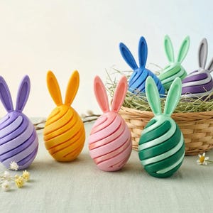 May include: A collection of colorful Easter egg decorations with bunny ears. The eggs are in shades of purple, yellow, pink, blue, green, and gray, with a spiral design. Some eggs are in a wicker basket filled with hay.