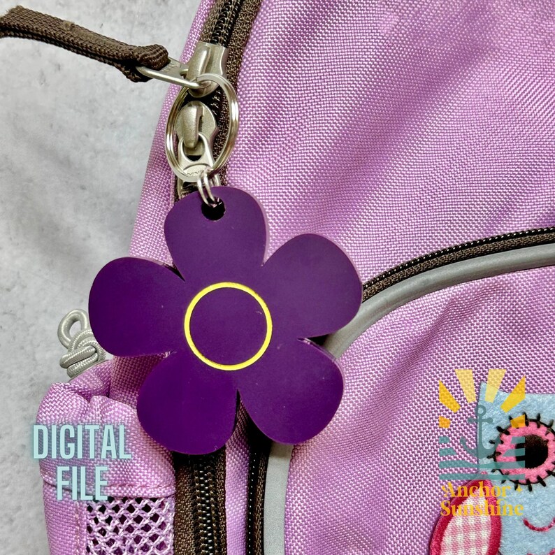 May include: A purple flower-shaped keychain with a gold center ring hangs from a silver clasp attached to a purple backpack. The words "DIGITAL FILE" are printed on the backpack. The keychain is a decorative accessory.