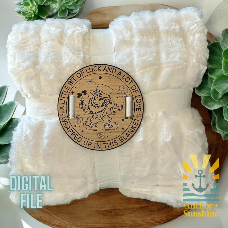May include: A white fuzzy blanket with a wooden circle attached to it. The circle has a leprechaun design and the text "A little bit of luck and a lot of love wrapped up in this blanket".