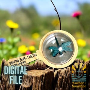 May include: A wooden magnifying glass with a clear plastic lens, showing a blue dragonfly inside. The handle is engraved with the text "You're Bug-Tastic from-Ryker". The magnifying glass is sitting on a tree stump with a blurred background of flowers.