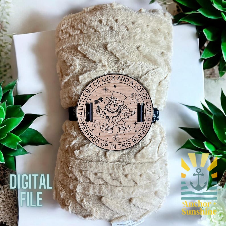 May include: A beige plush blanket with a wooden circle attached to it. The circle has a design of a leprechaun holding a four-leaf clover and the text "A little bit of luck and a lot of love wrapped up in this blanket".
