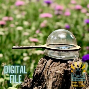 May include: A wooden bug catcher with a clear plastic dome. The bug catcher has a handle with the text "YOU'RE MY FAVORITE" on it. The bug catcher is sitting on a tree stump in a field of flowers.