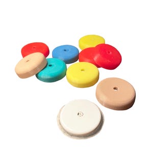 Può includere: Una collezione di dieci oggetti circolari a forma di disco in vari colori, tra cui rosso, blu, giallo, verde acqua, beige e bianco. Ogni disco presenta un piccolo foro centrale sulla superficie piatta e una sottile trama a strati.