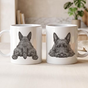 May include: Two white ceramic mugs featuring a detailed black and white illustration of a Scottish Terrier. The left mug shows the dog from behind, while the right mug displays the dog facing forward with its head resting on its front paws.