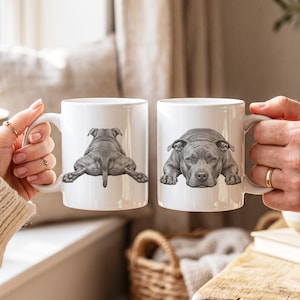 Puede incluir: Dos tazas de cerámica blanca con una ilustración detallada en blanco y negro de un perro pitbull. Una taza muestra al perro desde una vista trasera, mientras que la otra muestra al perro desde una vista frontal, apoyando su cabeza en sus patas.