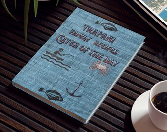 May include: A blue linen-textured cookbook with the title "Trapani Family Recipes Catch of the Day" in white and red lettering. The cover features illustrations of a fish, a crab, an anchor, and a person fishing from a boat.