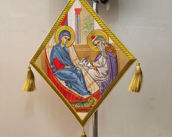 May include: Embroidered religious icon featuring two figures with halos, in blue, red, and purple, within a diamond-shaped frame. The frame is gold with a gold tassel at each corner. A gold ribbon is attached at the top.