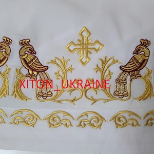 May include: White fabric with gold and maroon embroidered peacocks and floral designs. The embroidery includes crosses and the text "KITON_UKRAINE" in red. The design is likely for religious garments or decor.